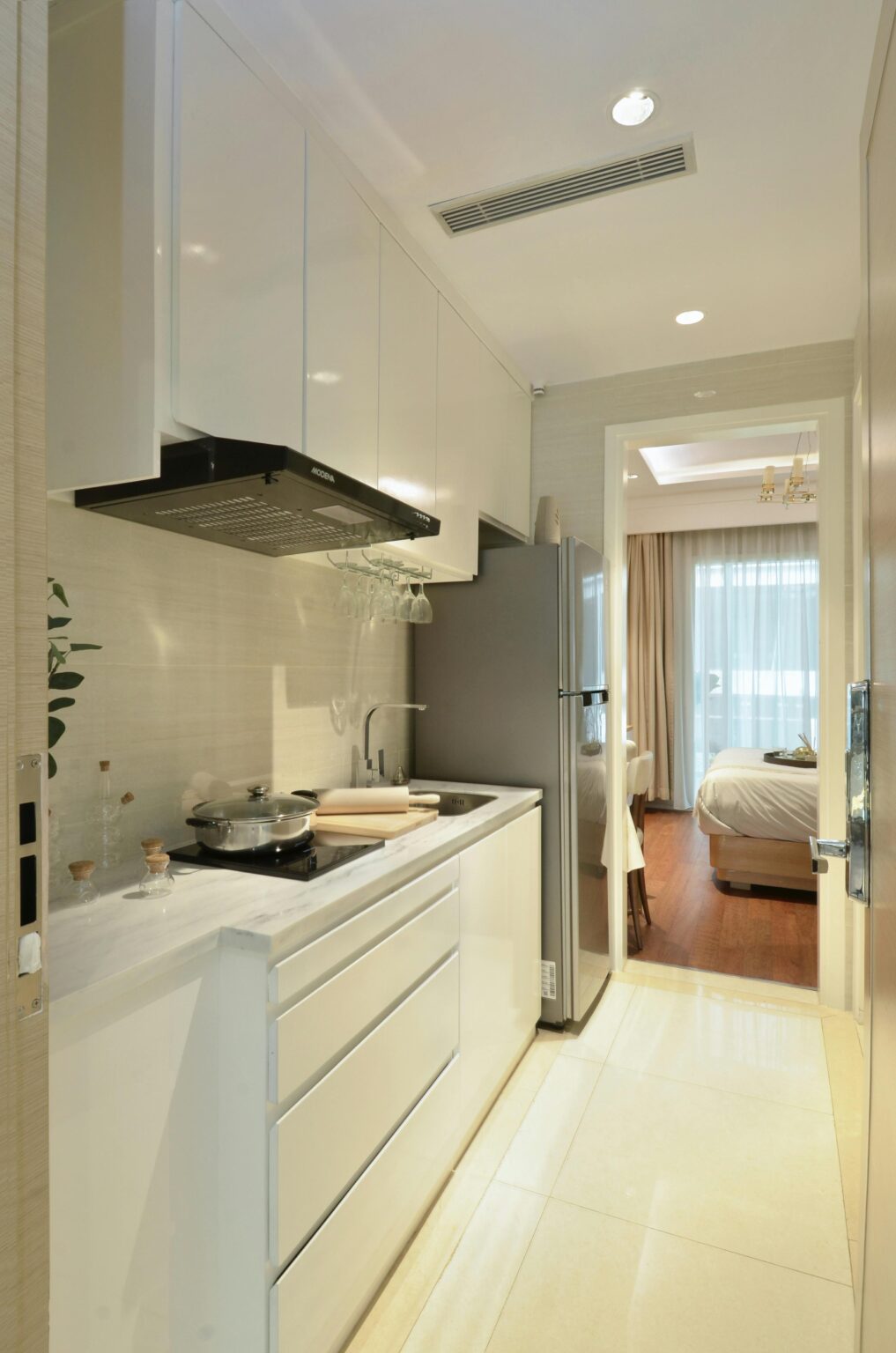 Modern white kitchen with sleek cabinets and stainless steel appliances, leading to a bright living area.